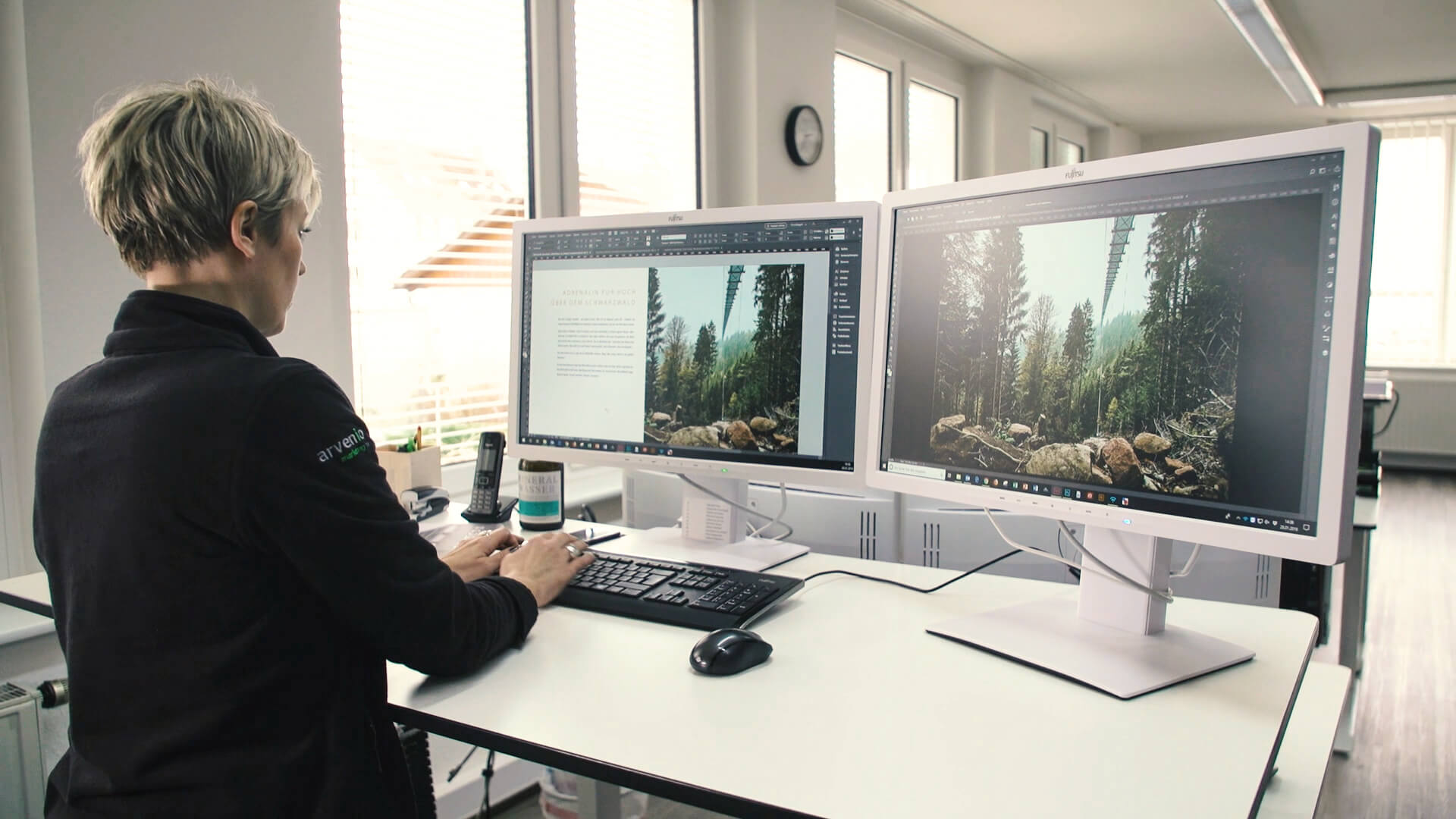 Frau sitzt im Buero an zwei Computern